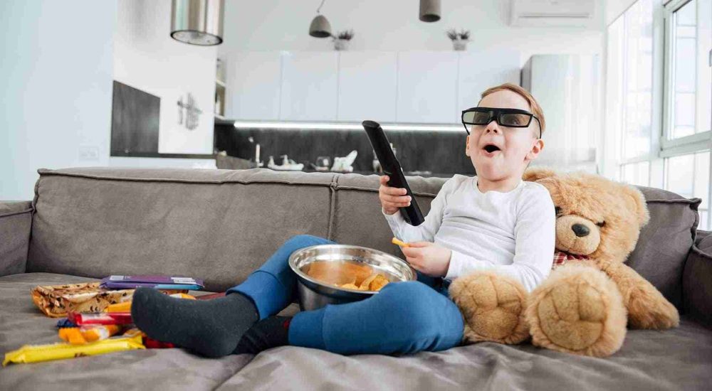little-boy-enjoying-tv-time-with-teddy-bear-and-snacks-SBI-303737309
